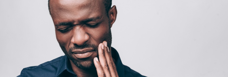 Man in need of emergency dentistry holding cheek in pain